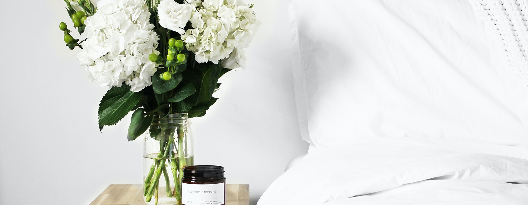 bed with white sheets next to nightstand with white flowers